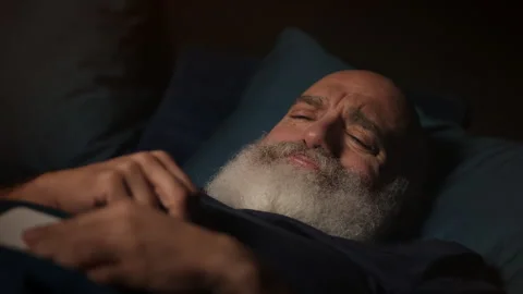 Unhappy middle-aged man reads upsetting message on phone in bed, insomnia Stock Footage 346714667
