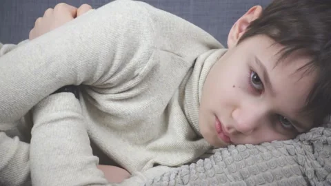 Unhappy sad young boy lying on couch at home. Child looking angrily direct to Stock Footage 148079853