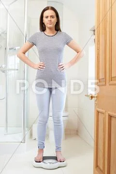 Unhappy Teenage Girl Standing On Bathroom Scales Stock Photos