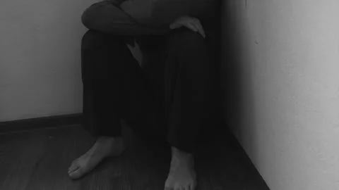 Unhappy unrecognizable man sitting in the corner of the room and holding his Stock Footage 273688026