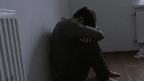 Unhappy unrecognizable man sitting in the corner of the room and holding his Stock Footage 273688216