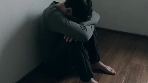 Unhappy unrecognizable man sitting in the corner of the room and holding his Stock Footage 273806664