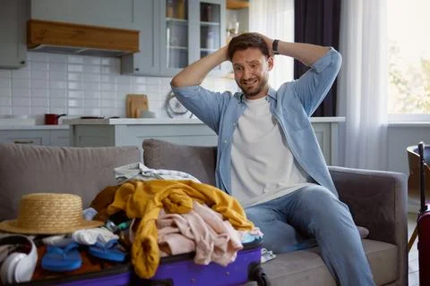 Unhappy worried man looking on stack of clothing in opened travel suitcase Stock Photos