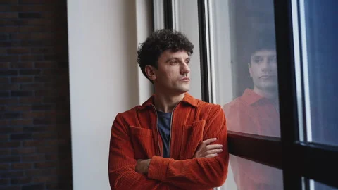 Unhappy young man with folded arms looking out the window, depression concept Stock Footage 337908482