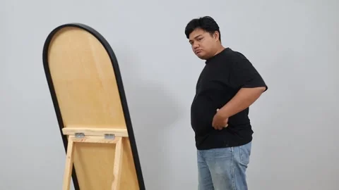Unhappy Young plus-size Asian man looking in mirror, feeling sad about his body Stock Footage 342283105