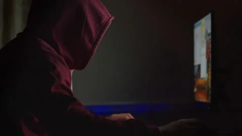 Unidentified man in a hood sits at a computer monitor at night Stock Footage 148757038