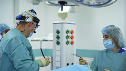 Uniformed surgeon with device glasses on his head applies metal tools.  Stock Footage 221114567
