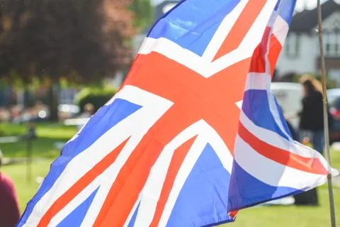 Union Jack flag flying in front of VE Day celebrations at a social distance s Stock Photos