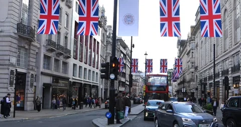 Union Jack flags over busy London street with red bus and evening traffic Stock Footage 321032456