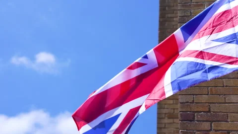 Union Jack flying in the wind against blue sky and brick wall corner Video stock 240440642