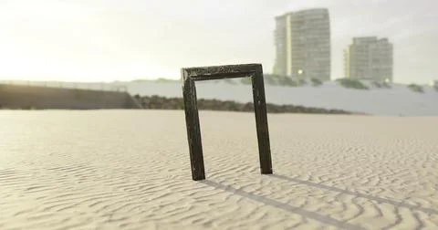 Unique black frame standing alone on sandy beach at sunset near buildings Ilustración de archivo