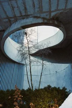 A unique concrete design features a large circular opening above. A few trees Stock Photos