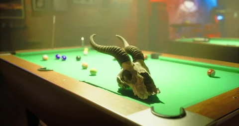 Unique decor features a ram skull on a vibrant pool table in low light Stock Footage 327793941