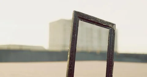 Unique empty picture frame placed outdoors with distant buildings in backgrou Ilustración de archivo