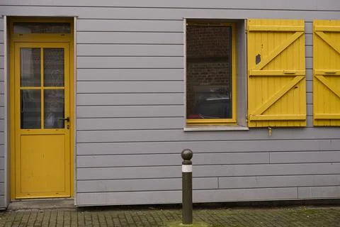 A unique gray wall with a vibrant yellow door and matching shutters adds char Stock Photos