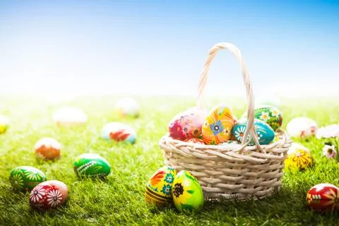 Unique hand painted Easter eggs in basket and lying on grass, blue sky Stock Photos