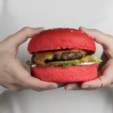 Unique red burger in hands with cheese and lettuce displayed close Stock Photos