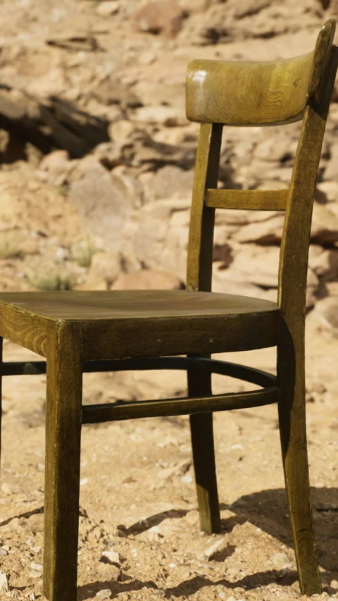 Unique rustic chair positioned in a sandy landscape surrounded by rocks Stock Footage 319066106