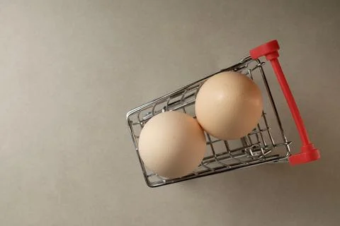 Unique shopping experience with eggs in a small cart on a simple background Stock Photos