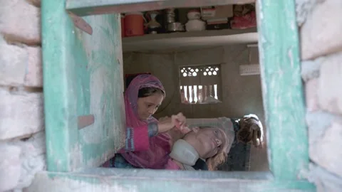 Unique shot through green window shows tribal sisters, one disabled, getting rea Stock Footage 154997997