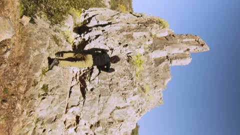 Unique Vertical Shot of a Climber in Black Ascending a Rocky Cliff, Exhibiting Stock Footage 275039072
