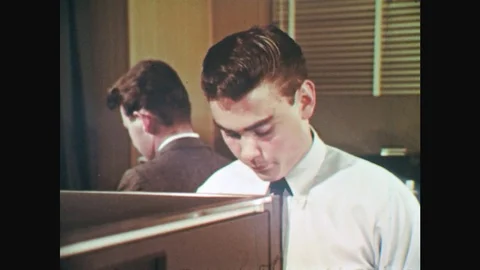 UNITED STATES: 1960s: boy in office. Man and girl pile up papers from machine. Stock Footage