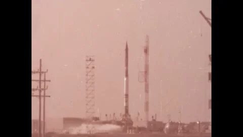United States 1960s: A rocket stands upright on its launchpad beside a tall Stock Footage 247780098