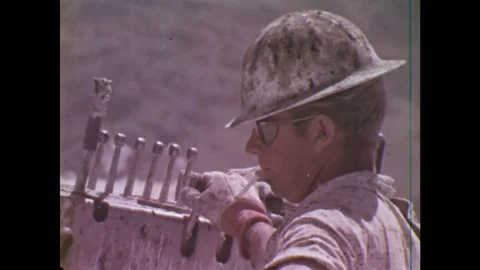 UNITED STATES: 1970S: man operates machinery on rock. View through trees. Truck Stock Footage