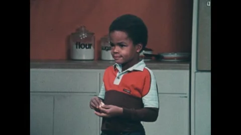 UNITED STATES 1980s: Boy eats a piece of candy in a kitchen. Girl bites a slice Stock Footage 314142959