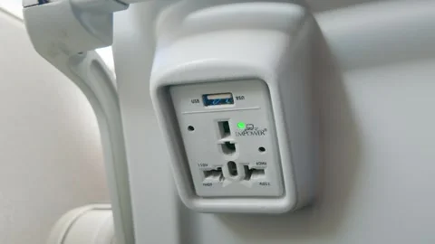 Universal power outlet and USB charging port mounted on an airplane seat back Stock Footage 346659218