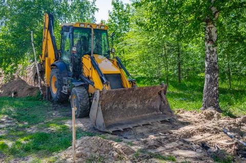 Universal wheel backhoe loader digging a trench for the laying of pipes betwe Foto stock