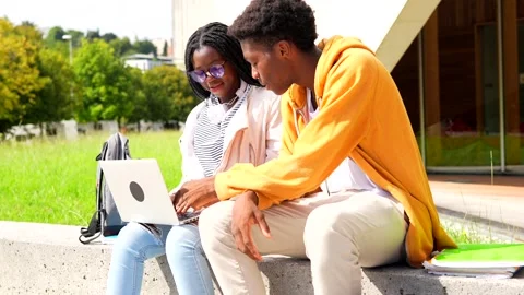 University friends using laptop sitting outside the campus Stock Footage 282958947