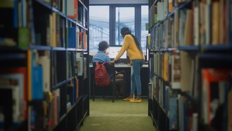 University Library: Boy Uses PC at His Desk, Smart Girl Classmate Explains Him Stock Footage 126914092