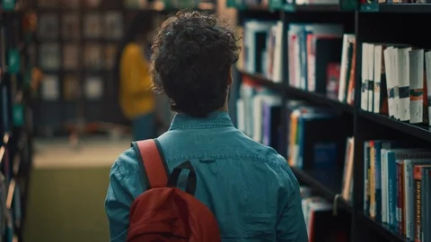 University Library: Student Walks Between Bookshelves Searching for Right Book Stock Footage 126916565