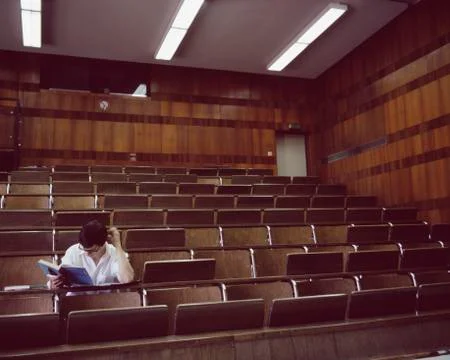 University student sitting in an empty lecture hall reading a text book Stock Photos
