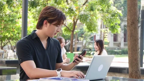 University Student Using Laptop and Smartphone on Campus Outdoor Table Vídeos de archivo 330035418