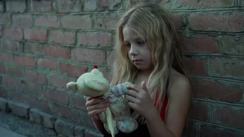 An unkempt little girl from a poor family plays with her toy against the back Stock Footage