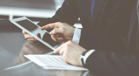 Unknown businessmen using tablet computer and work together at the glass desk in Stock Photos