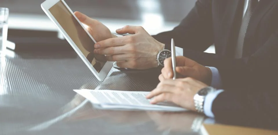 Unknown businessmen using tablet computer and work together at the glass desk in Stock Photos