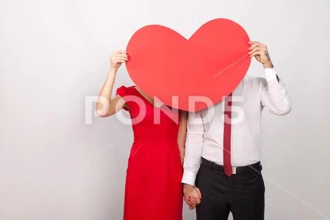 Unknown couple hide and seek behind big red heart Stock Photos