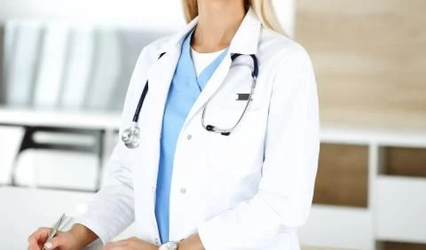 Unknown female physician is standing at her workplace near desktop computer Stock Photos