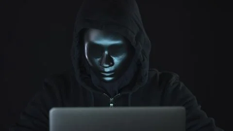 Unknown hacker or robot wearing black clothes and mask uses the computer Foto stock