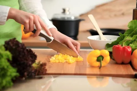 Unknown human hands cooking in kitchen. Woman slicing yellow bell pepper Stockfoto's