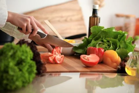 Unknown human hands cooking in kitchen. Woman slicing red tomatoes. Healthy meal Stockfoto's