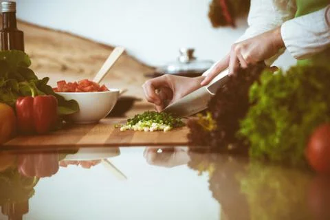 Unknown human hands cooking in kitchen. Woman slicing green onion. Healthy meal 库存照片