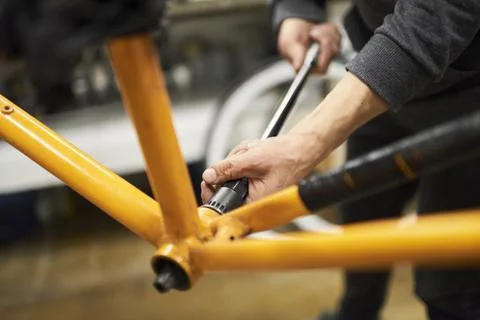 Unknown man disassembling an orange bike to paint it at his repair shop. Stock Photos