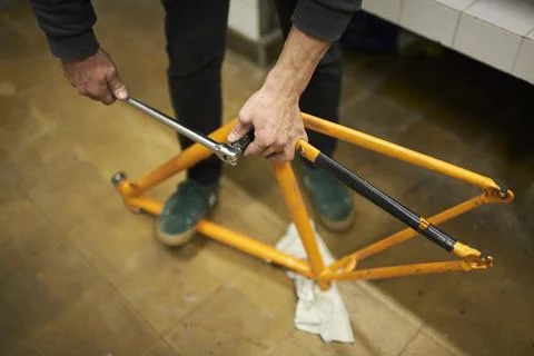 Unknown man disassembling an orange bike to paint it at his repair shop. Stock Photos