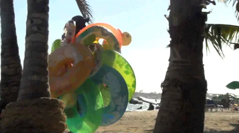 Unknown man passes carrying tons of floaty toys on a beach Stock-Footage 38320313