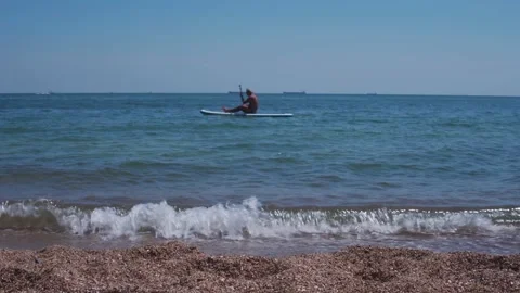 Unknown man sits on a SUP board and paddling along the seashore Stock Footage 159126865