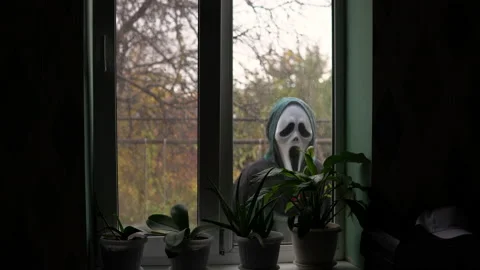An unknown person appears outside the window wearing a screaming mask. Maniac in Stock Footage 163778380
